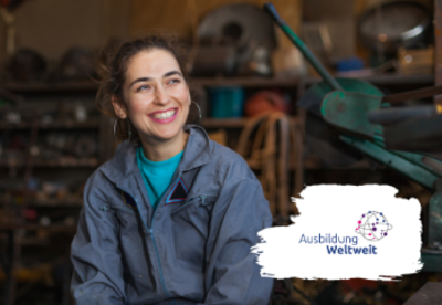 Foto: junge Auszubildende sitzt mit strahlendem Lachen in der Werkstatt. Das Logo AusbildungWeltweit am rechten Bildrand.